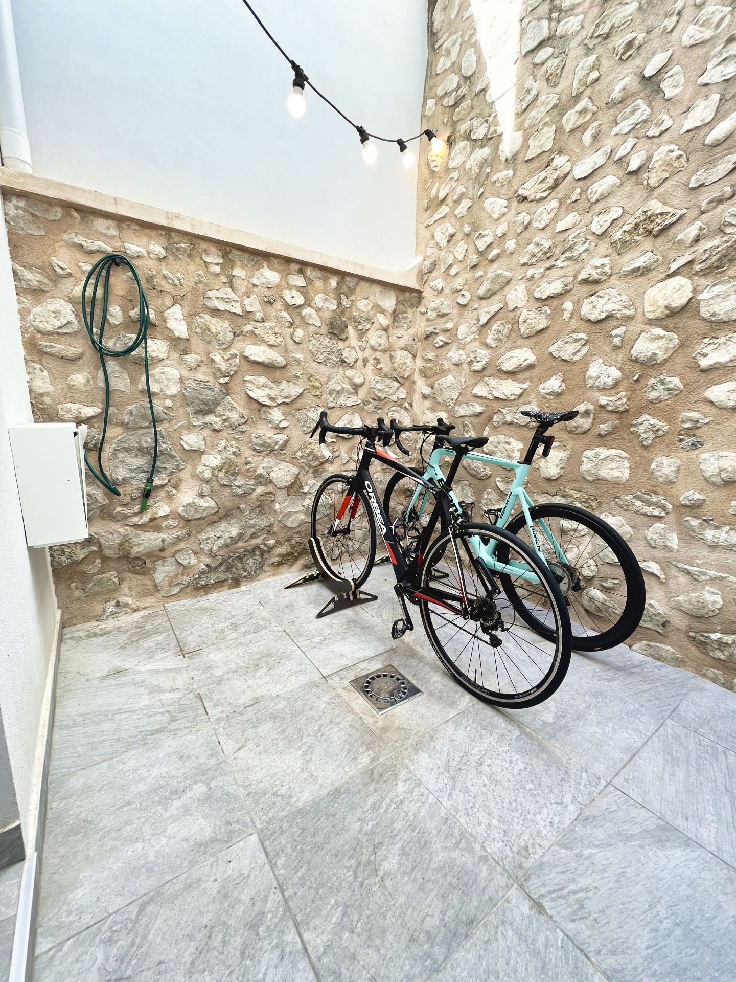 Patio interior con paredes de piedra y manguera de lavado, ideal para limpiar bicicletas en una casa rural para ciclistas