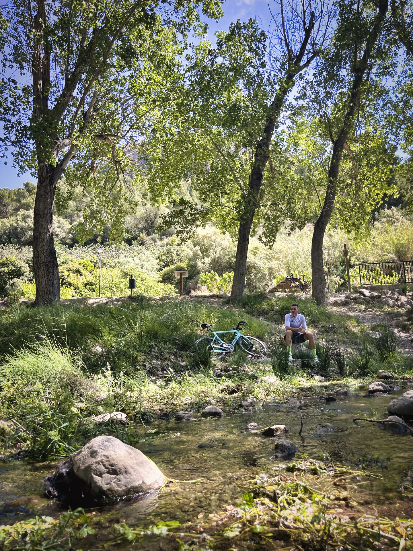 Ciclista descansando junto al río Bolulla y árboles en una ruta de cicloturismo por el interior de la Costa Blanca