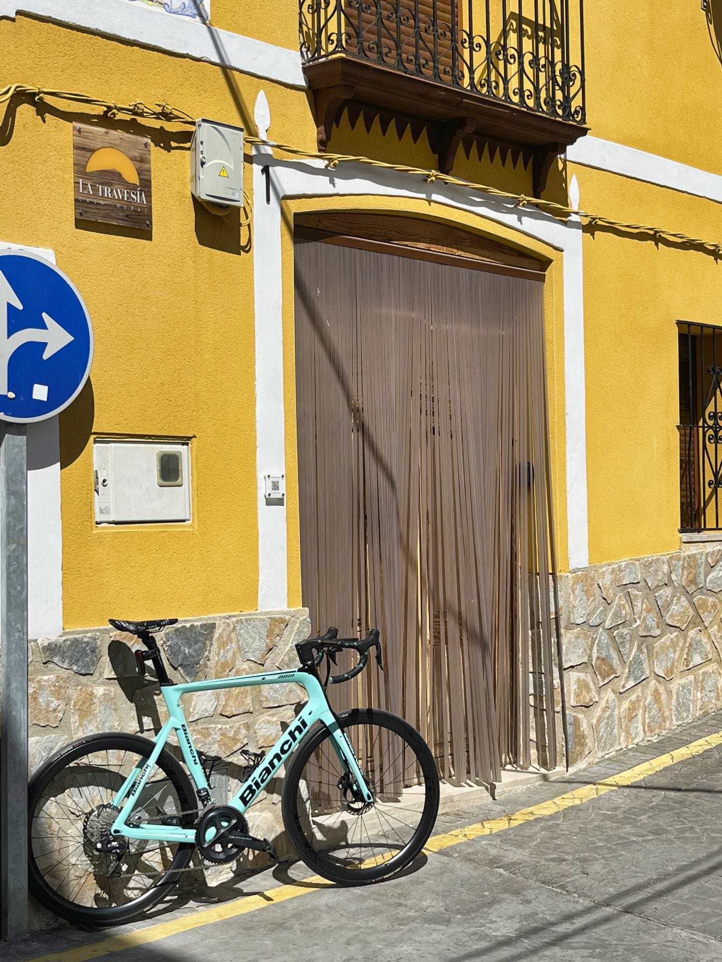 Bicicleta de ruta celeste apoyada en el zócalo de piedra de la fachada de una casa rural orientada al turismo de ciclismo